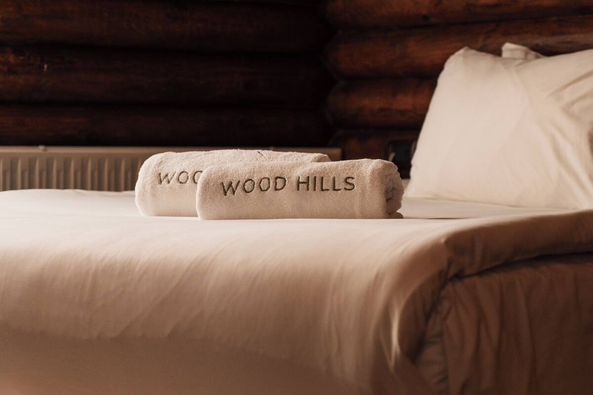 A neatly made bed with two towels labeled "WOOD HILLS" and a white pillow.