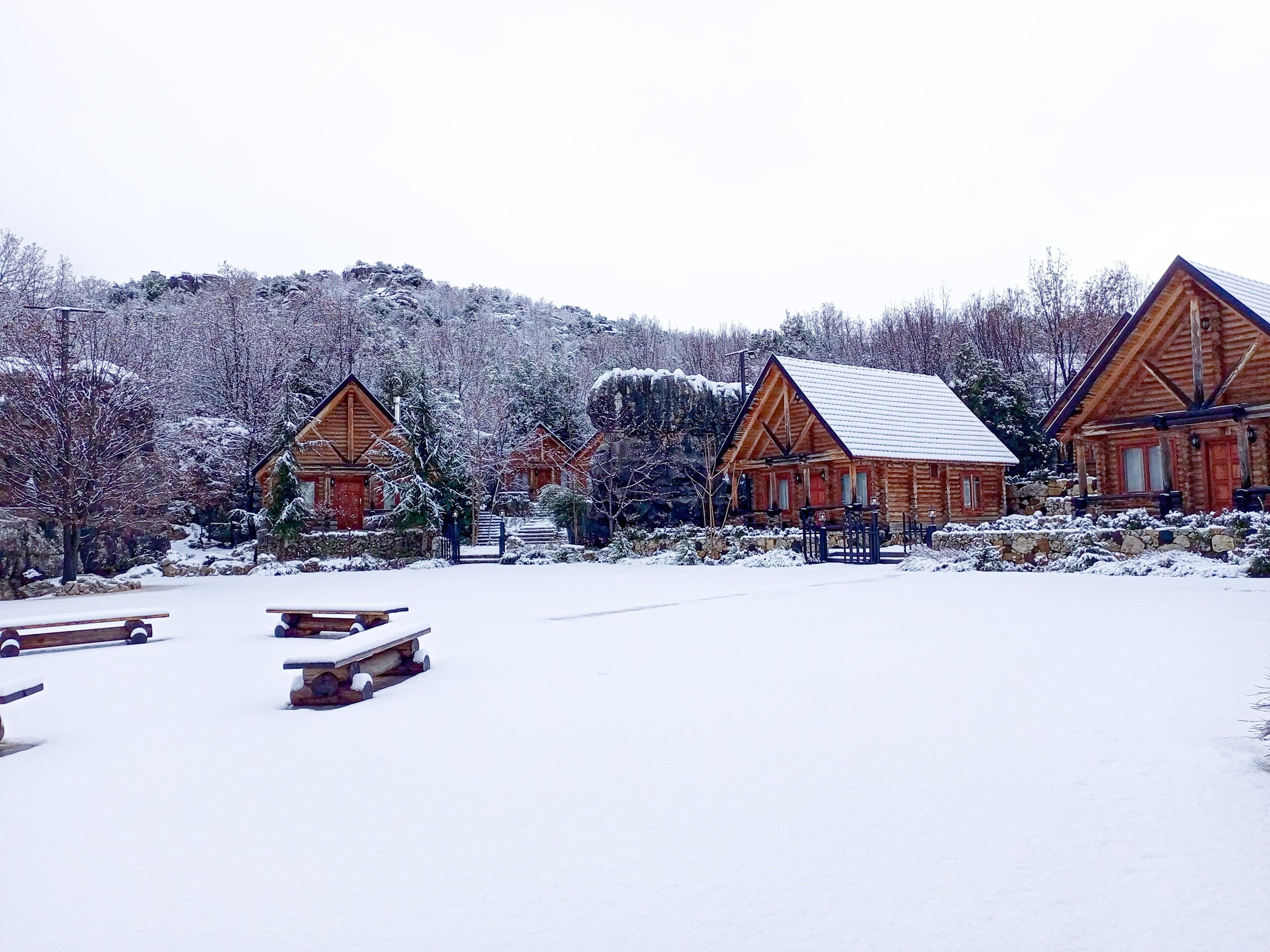 A snow-covered lodge with wooden cabins, a stone wall, and a snow-covered landscape.