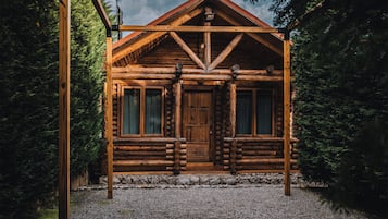A log cabin with a symmetrical facade, a central door flanked by windows, and a stone foundation.
