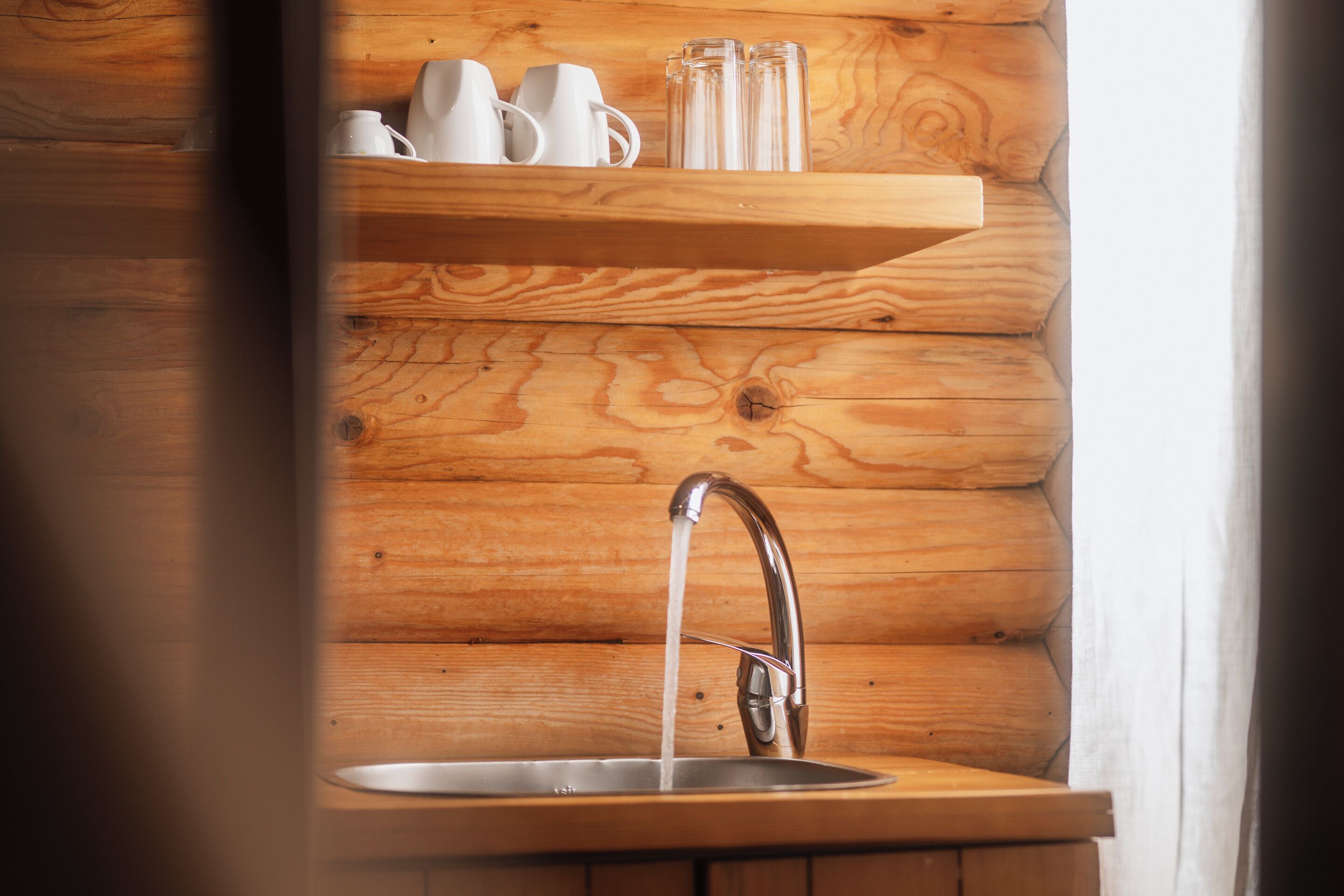 L’intérieur d’une cabane en bois, avec une étagère en bois au-dessus d’un évier où coule l’eau.