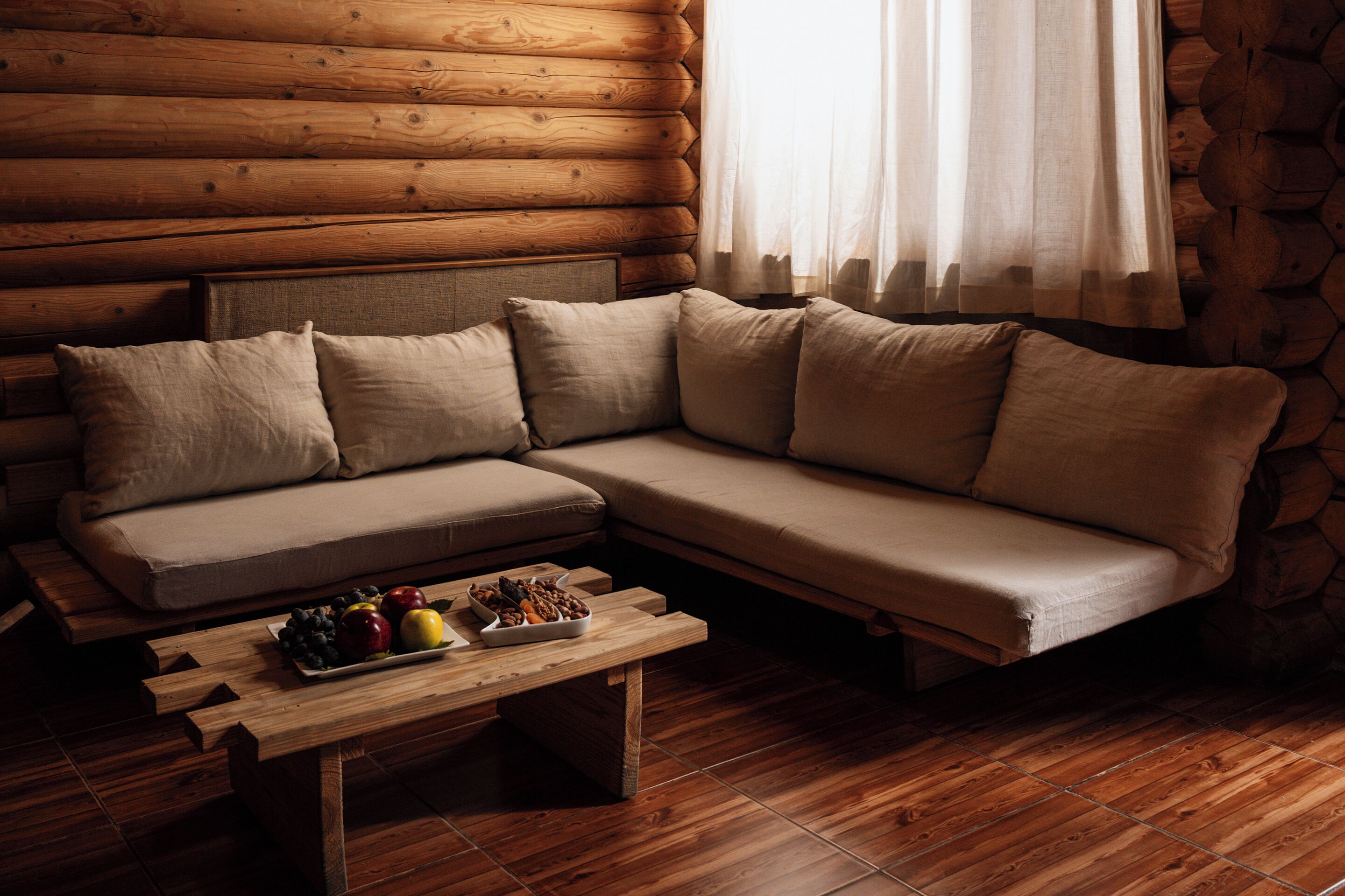 A log cabin interior with a sofa, wooden flooring, and a table with fruit.