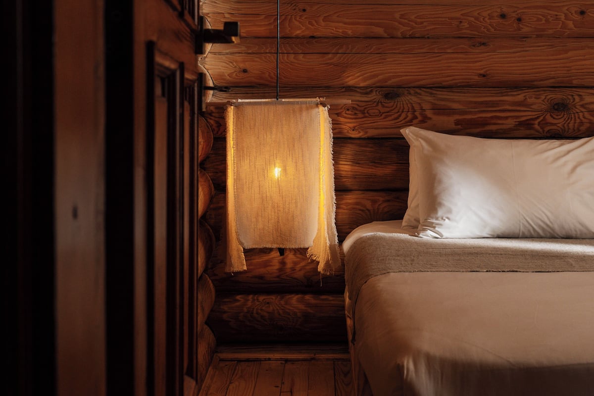 A cozy cabin-style room with a wooden ceiling, a bed with white bedding, and a hanging light fixture.