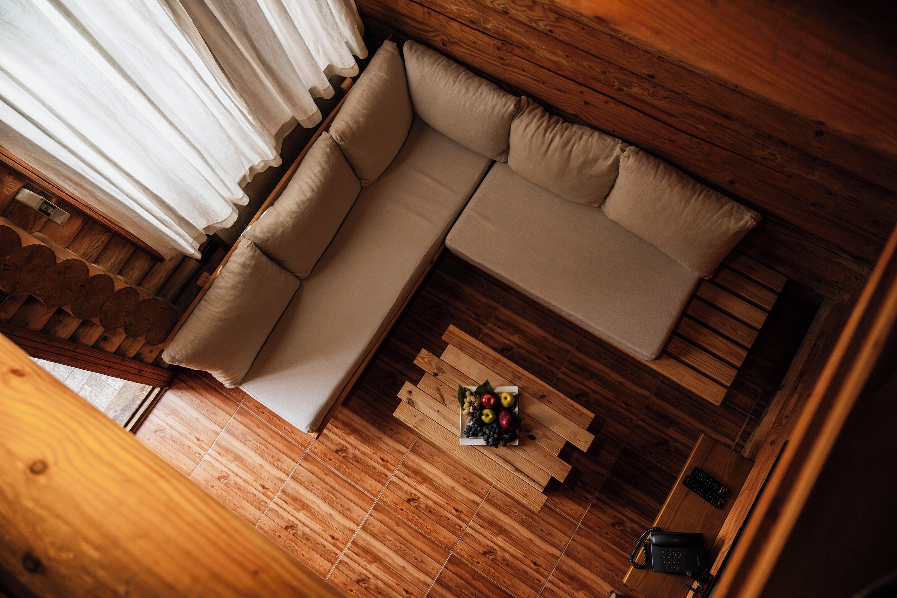 A wooden interior with a beige sofa, a wooden coffee table with fruit, and a wooden desk with a telephone.