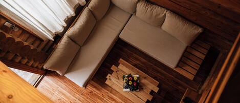 Un interior de madera con un sofá color beige, una mesa de centro de madera con fruta, y un escritorio de madera con un teléfono.