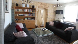 Ein Wohnzimmer mit zwei Sofas, einem Glastisch, einem Bücherregal, einem Kamin und einem Fernseher.