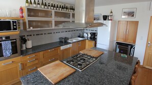 Eine moderne Küche mit Granit Arbeitsplatten, Holzschränken, einer Edelstahl-Dunstabzugshaube und einer Weinsammlung an der Wand.