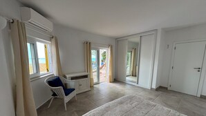 Un dormitorio con cama, escritorio, silla, armario y puerta corrediza de vidrio que da a un balcón.
