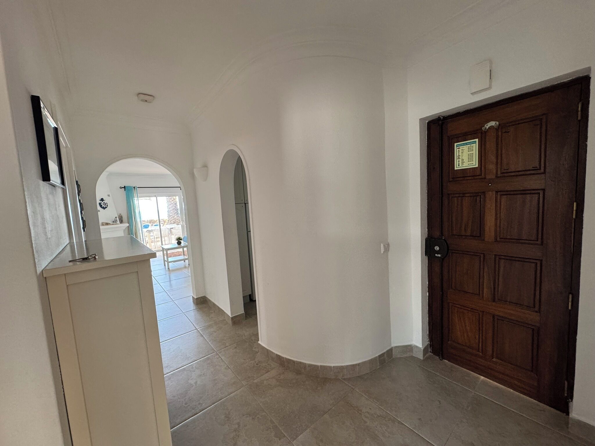 A hallway with a wooden door, a white wall, and a tiled floor.