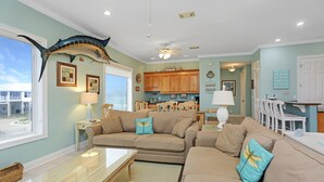 A living room with a large fish mounted on the wall, a beige sofa, a glass coffee table, and a view of the ocean through a window. - 5BR Gulf Front w/Private Pool Near Rock Wall ~ Beach Blessing (Cape San Blas)