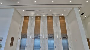 A modern elevator area with three elevators, each marked with a digital display showing the floor number. - Abdali Views Apartments (Amman)