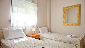 A bedroom with two beds, a bedside table with a lamp, a mirror, and a window with sheer curtains. - Olive Garden house (Καμηλάρι)