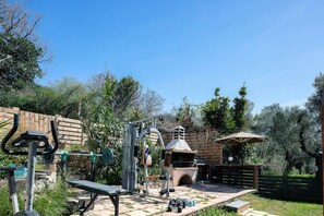 Ein Outdoor-Fitnessbereich mit Trainingsgeräten, einer Bank und einem Grillplatz.