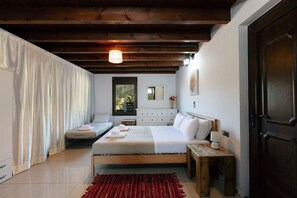 Une chambre avec un grand lit, deux petits lits, un banc en bois, un tapis rouge, une fenêtre avec vue et une porte en bois sombre.