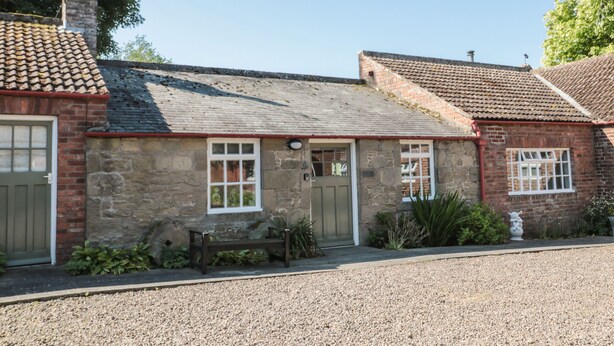 A stone building with a tiled roof, a front door, and a bench in front.