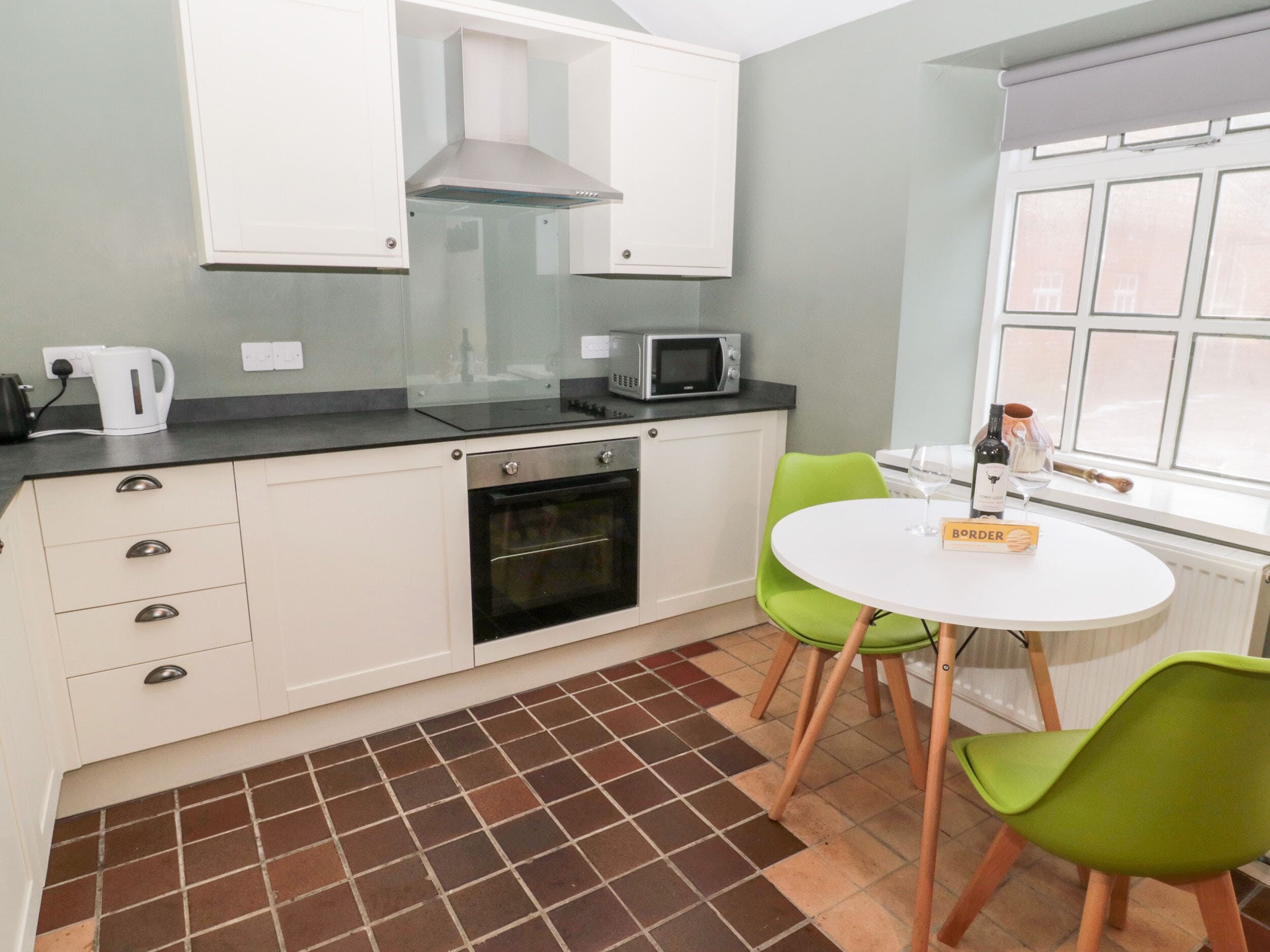 A compact kitchen with white cabinets, a built-in oven, a microwave, and a window with blinds.