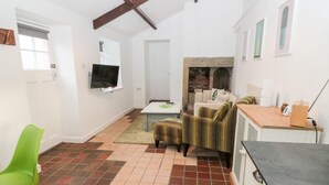 A spacious living area with a tiled floor, a television mounted on the wall, a fireplace, and a dining area with a table and chairs.