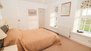A bedroom with a bed, a lamp, a window with a view, a radiator, and a door.