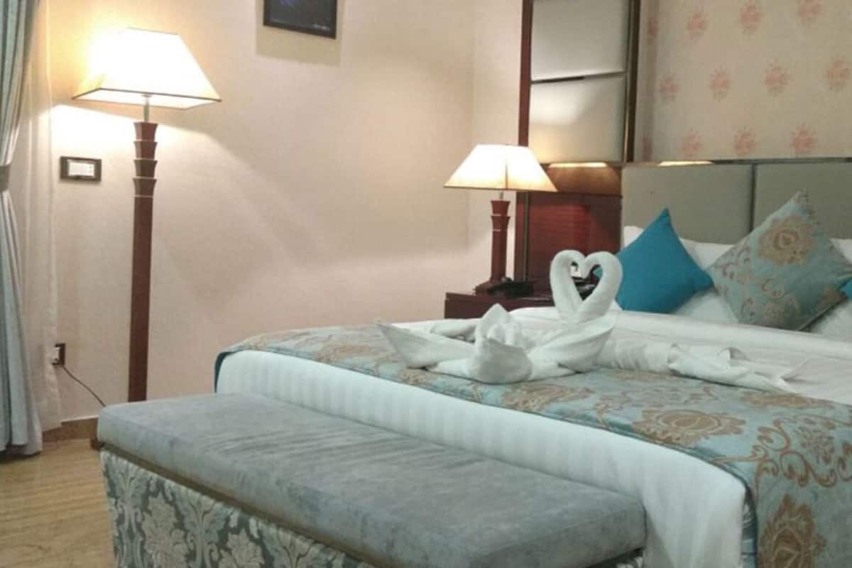 A hotel room with a bed, two bedside lamps, and a floral wallpaper.