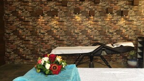 Une table de massage recouverte d’une serviette blanche, avec un bouquet de fleurs, dans une pièce dont un mur est en briques.