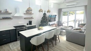 A modern kitchen with a central island, bar stools, a dining area, and a living space with a sofa and TV. - Luxury 5 Bedroom Home, 3 Minute Walk from the Beach (Dorado)