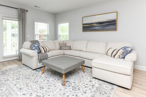 A modern living room with a sectional sofa, a grey ottoman, and a patterned rug.