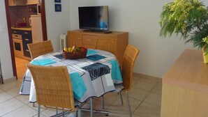 Un comedor con una mesa dispuesta para cuatro, un televisor sobre un mueble de madera y una planta a la derecha.