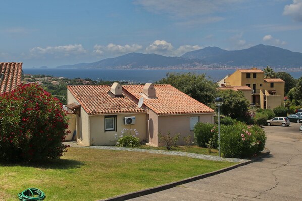 Un quartier résidentiel où les maisons sont dotées de toits en tuiles et offrent une vue dégagée sur la mer et les montagnes en arrière-plan.