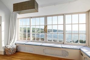 A room with a large bay window overlooking a scenic view of hills and water.