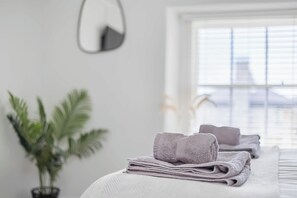 A hotel room with a neatly made bed, a potted plant, and a window with blinds. - NEW 2023 Beach House in Devon - Sleeps 10 (Bovisand)