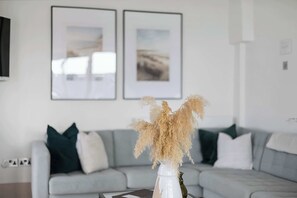 A living room with a grey sofa, green and white cushions, and a white vase with dried plants on a table. - NEW 2023 Beach House in Devon - Sleeps 10 (Bovisand)