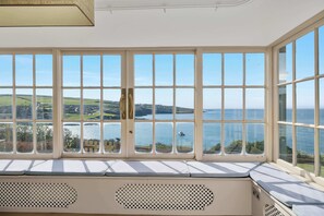 A bay window with multiple panes offering a view of a coastal landscape, including hills and a body of water. - NEW 2023 Beach House in Devon - Sleeps 10 (Bovisand)