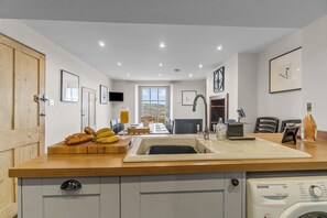 A modern kitchen with a built-in dishwasher, a sink, and a dining area with a table and chairs. - NEW 2023 Beach House in Devon - Sleeps 10 (Bovisand)