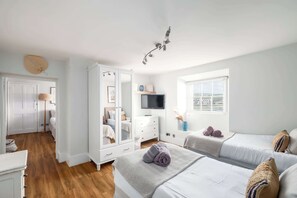 A bedroom with two beds, a wardrobe, a television, and a window with blinds.