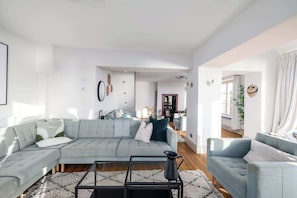 A modern living room with a sectional sofa, a coffee table, and a view into the kitchen and dining area. - NEW 2023 Beach House in Devon - Sleeps 10 (Bovisand)