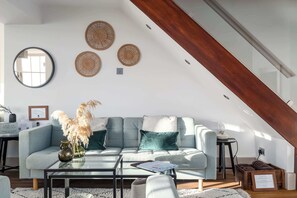 An attic room with a light grey sofa, a glass coffee table, and a wooden beam ceiling. - NEW 2023 Beach House in Devon - Sleeps 10 (Bovisand)