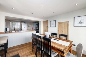 A modern kitchen with white cabinets, a wooden dining table, and black chairs. - NEW 2023 Beach House in Devon - Sleeps 10 (Bovisand)