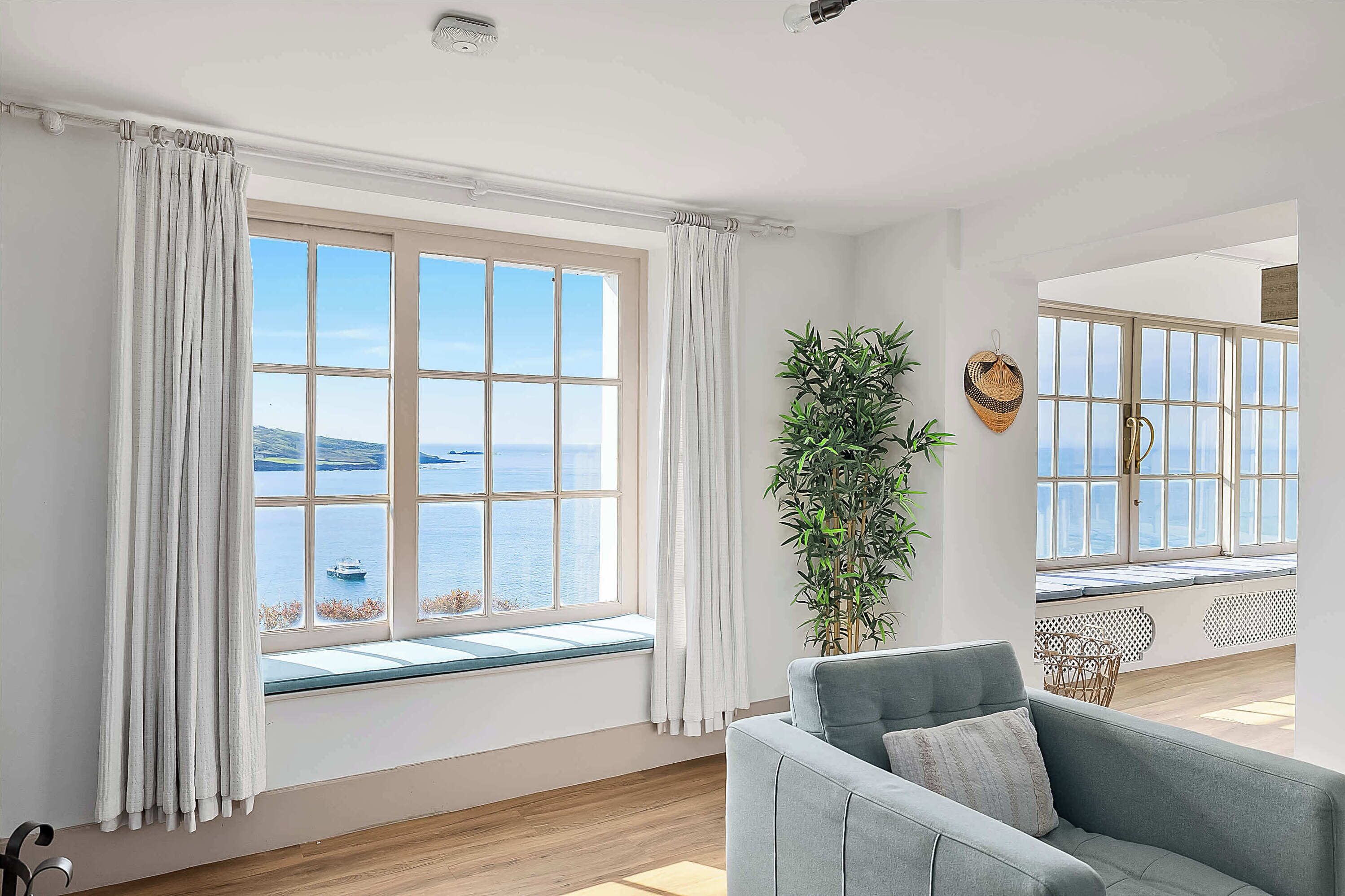 A room with large windows, a grey sofa, and a potted plant.
