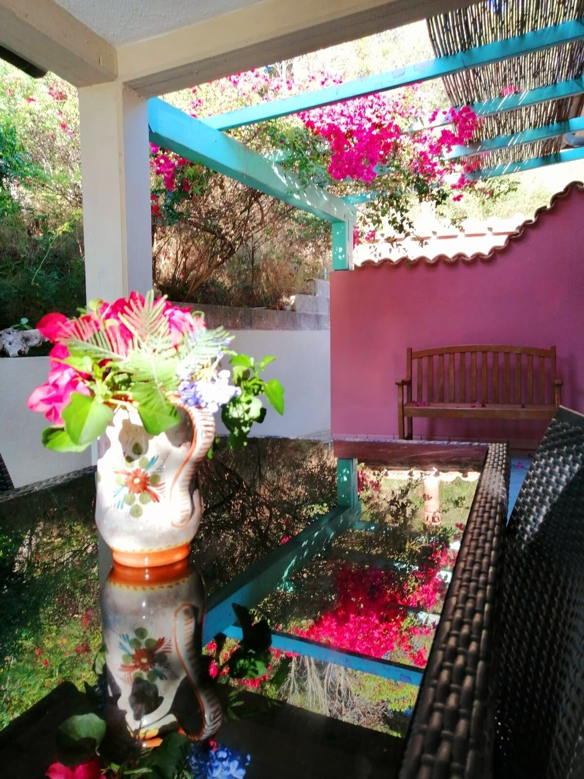Ein Glastisch mit Blumen in einer Vase, eine Bank und Blick auf einen Garten mit rosa Blumen.