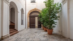 A narrow stone-paved courtyard with a staircase on the left, a large wooden door in the center, and potted plants on the right. - Torremuzza Home by Wonderful Italy (Palermo)