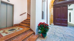 A staircase with a patterned floor leading to a door, a potted plant with red flowers, and a large dark wooden door. - Torremuzza Home by Wonderful Italy (Palermo)