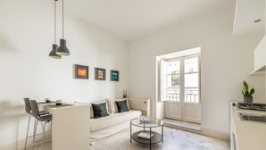 A modern living room with a sofa, two chairs, a glass coffee table, and a kitchen area with a stove. - Torremuzza Home by Wonderful Italy (Palermo)