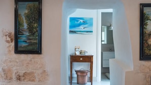Un couloir aux murs de pierre rustique, une table en bois surmontée d’un pot en cuivre, et des tableaux encadrés accrochés aux murs.