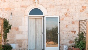 Un bâtiment en pierre avec une porte en bois et un panneau de verre. On y voit des plantes en pot et une lanterne posée sur le sol.