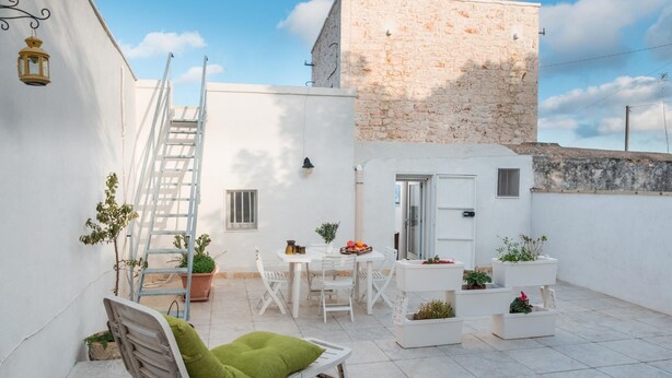 Une petite cour avec une chaise blanche, une table et des plantes en pot.