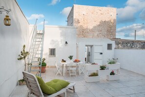 A small courtyard with a white chair, a table, and potted plants. - Sea and the City Apartment by Wonderful Italy (Ostuni)