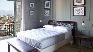 A bedroom with a large bed, a bench, a bedside table, and a view of the city through a balcony. - Eleganza nel Cuore di Napoli by Wonderful Italy (Naples)