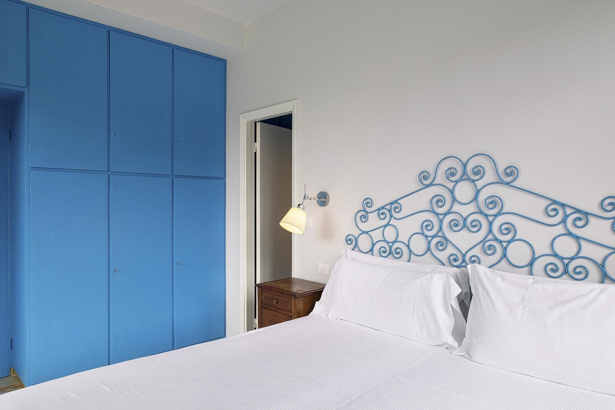 A bedroom with a bed, white bedding, a blue wardrobe, and a decorative metal headboard.