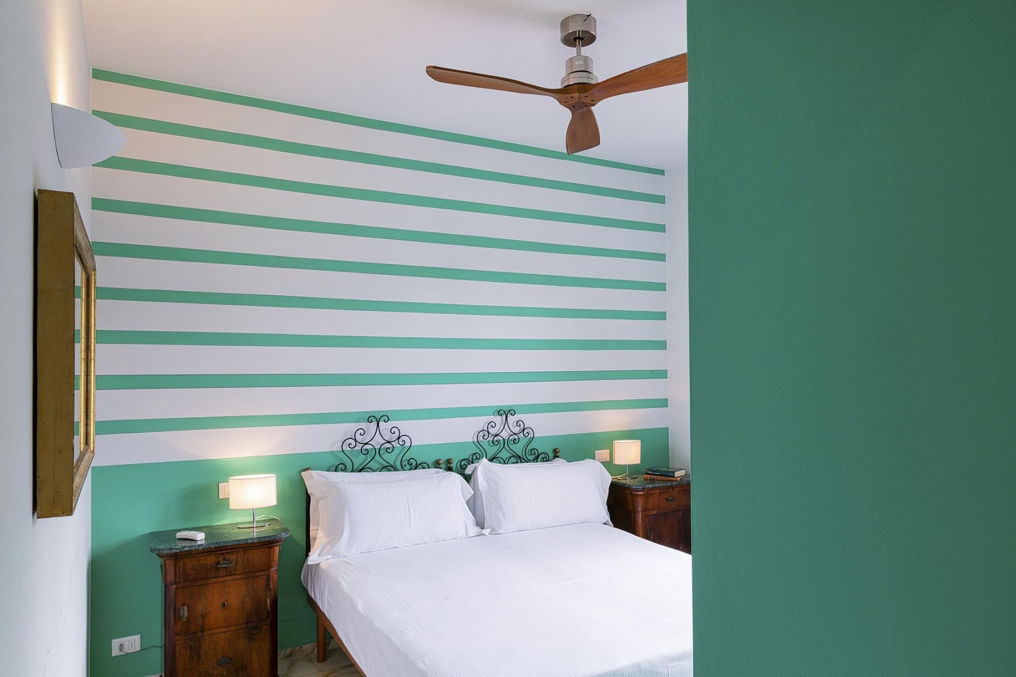 A room with a bed, a nightstand, a ceiling fan, and a wall with green and white stripes.