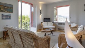 A spacious living room with wicker furniture, a flat-screen TV, and large windows offering a view of the landscape. - Appartamento a Villa Montuoro by Wonderful Italy (Rapallo)