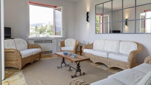 A living room with wicker furniture, a large window with a view, and a flat-screen TV. - Appartamento a Villa Montuoro by Wonderful Italy (Rapallo)